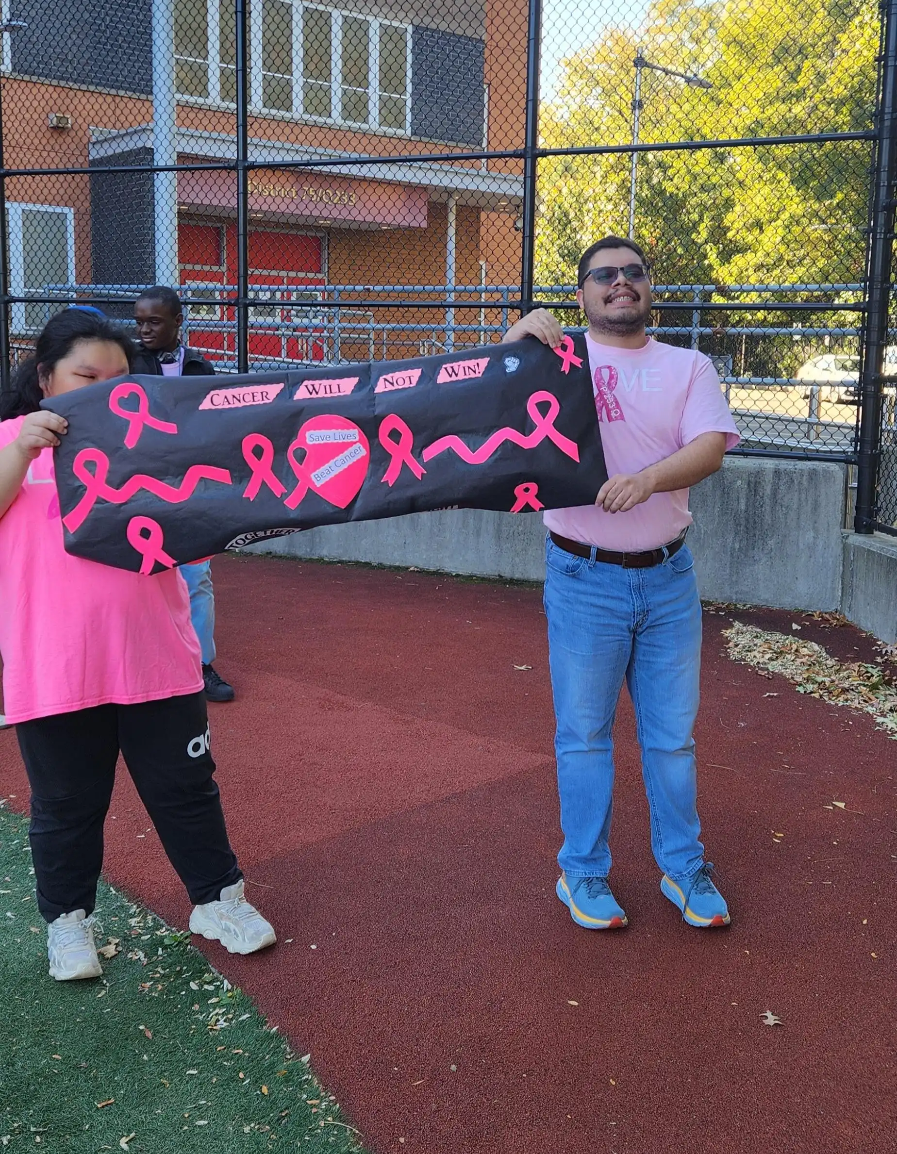 two students wearing pink holding a breast cancer fundraiser banner