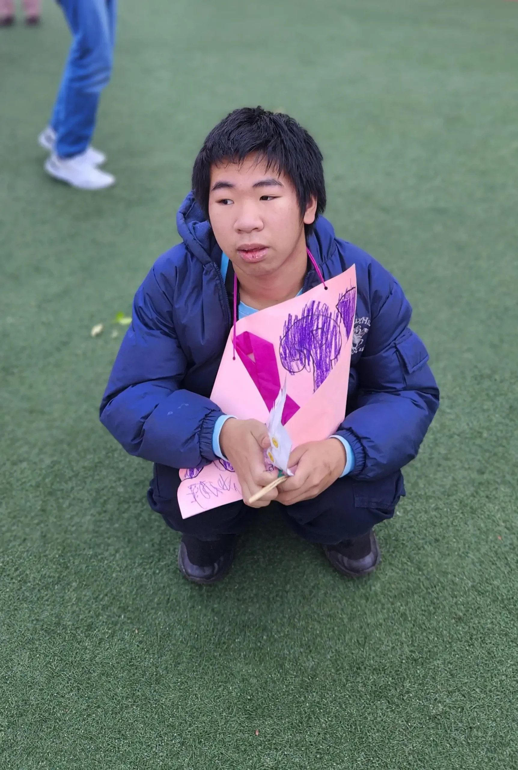 student sitting on grass wearing pink holding a breast cancer fundraiser banner