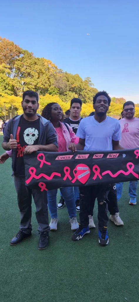 four students wearing pink holding a breast cancer fundraiser banner