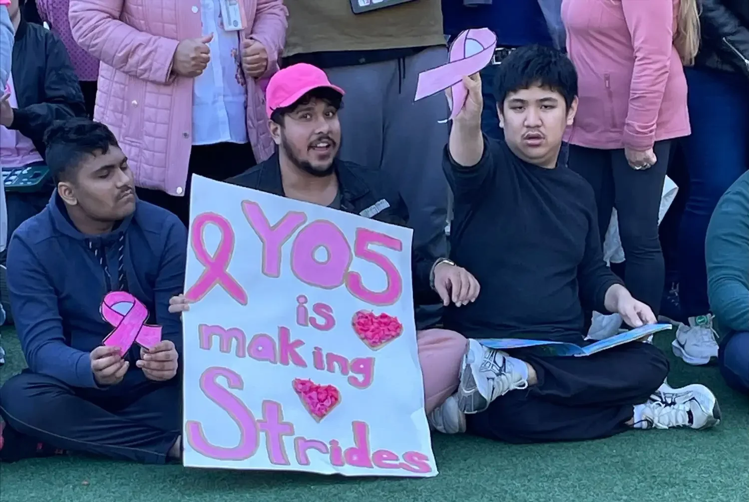 two students and their teacher wearing pink holding a breast cancer fundraiser banner