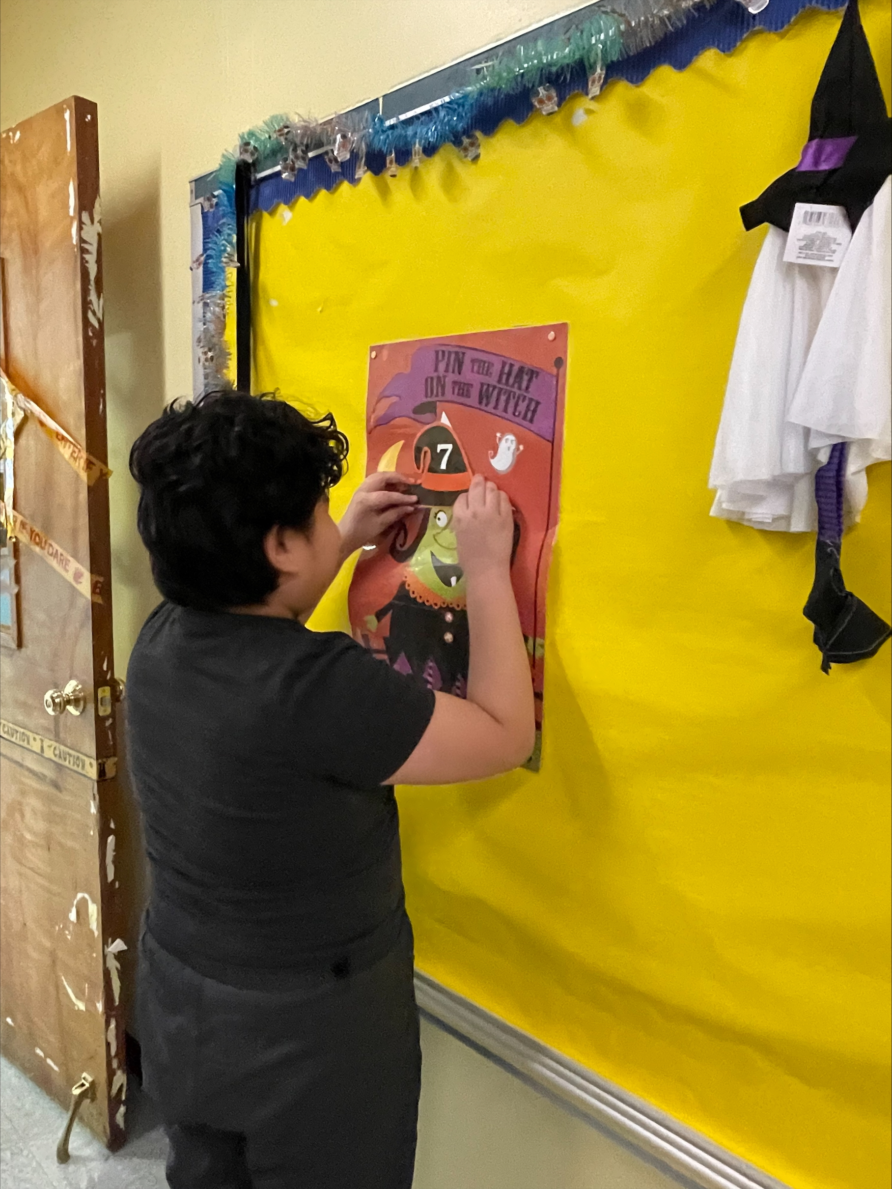 Student putting up fall decoration on a yellow bulletin board